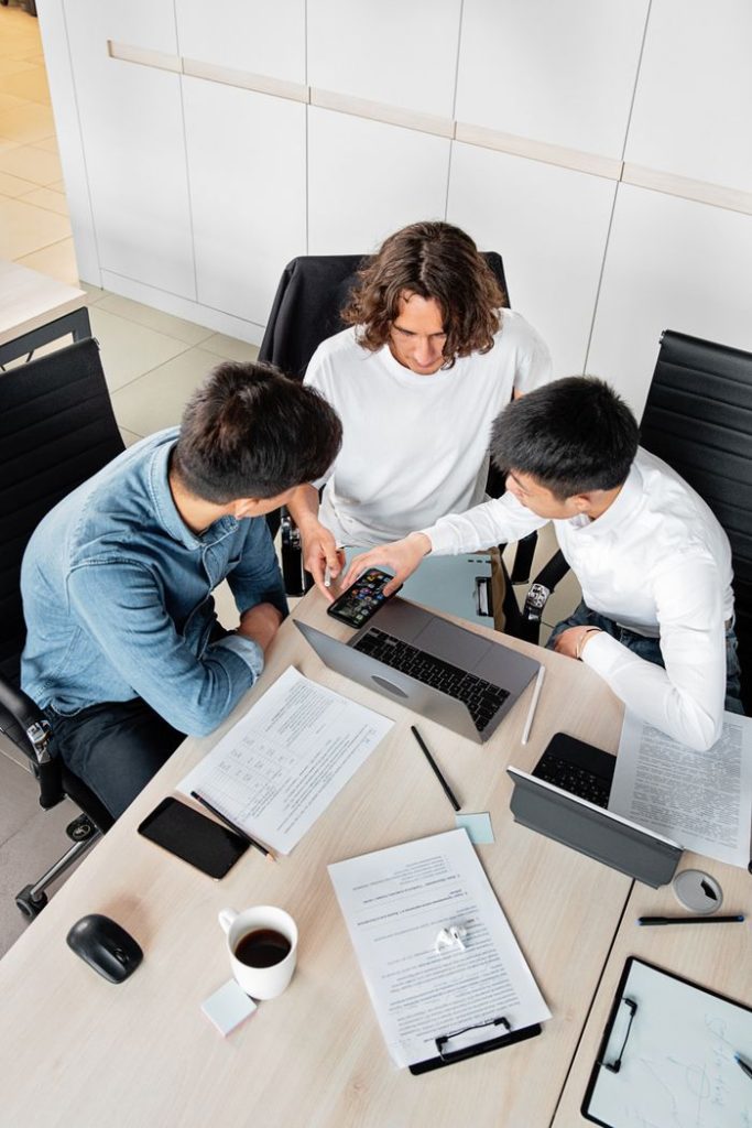 pexels photo 7988673 Overhead view of three colleagues collaborating at a desk with laptops and documents.